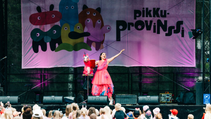 henkilö seisoo esiintymislavalla punertavassa mekossa esiintyen yleisölle.